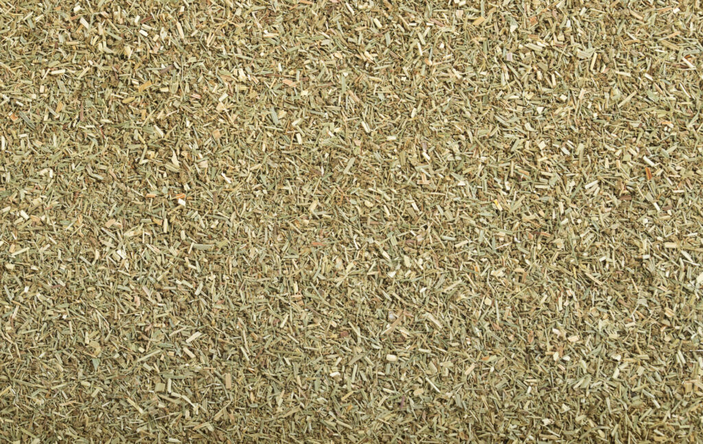 The image displays a close-up texture of dried herbs, predominantly green with some variation in color, likely used for culinary or medicinal purposes.