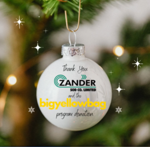 White Christmas ornament with writing that says "Thank you Zander Sod Co. Limited and BigYellowBag program donation with sparkling stars and a Christmas background
